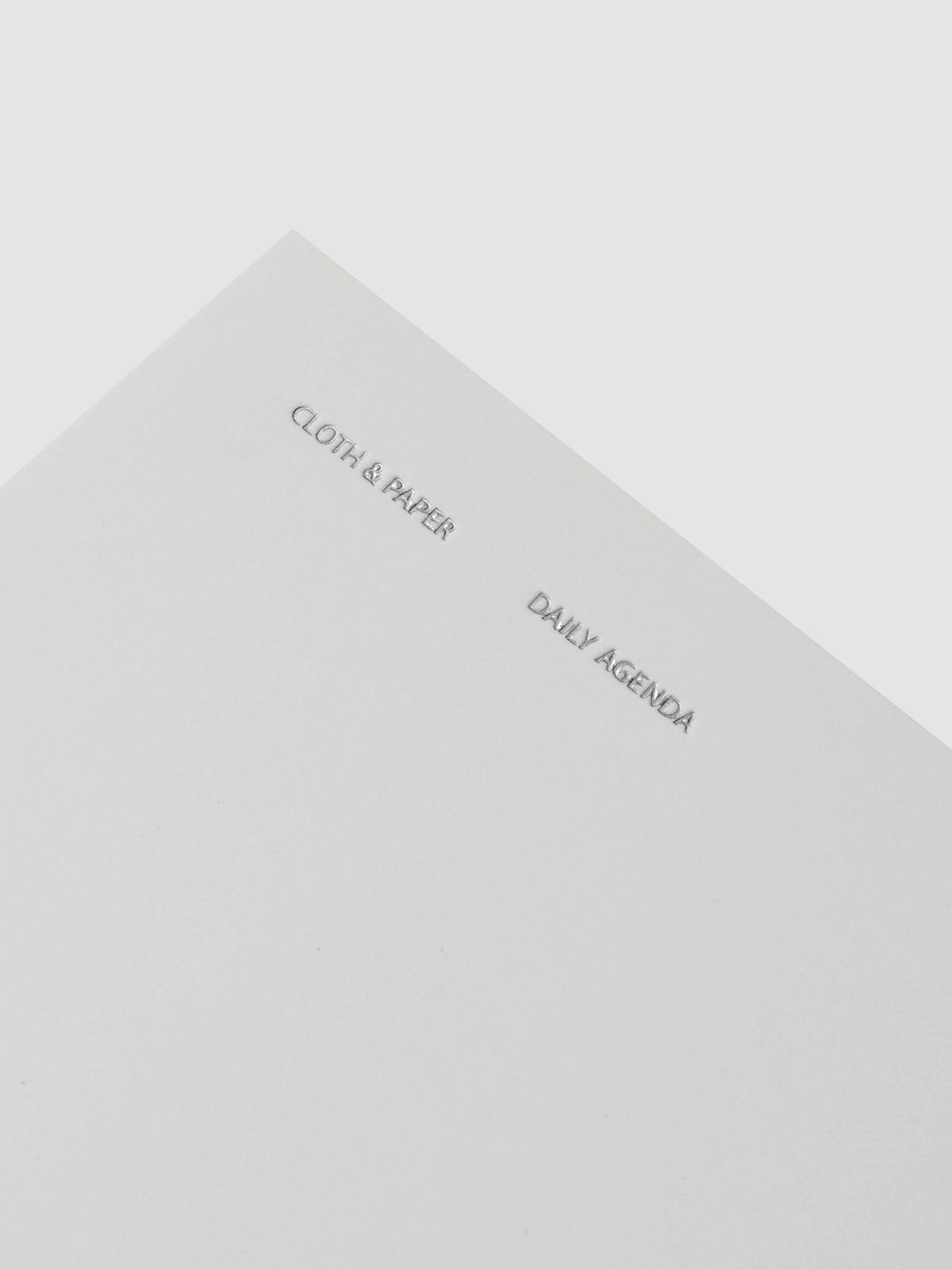 Close up of foil details on Travel Notebook | Pocket Plus | Aspen | Daily Agenda shown closed with packaging against a neutral background.