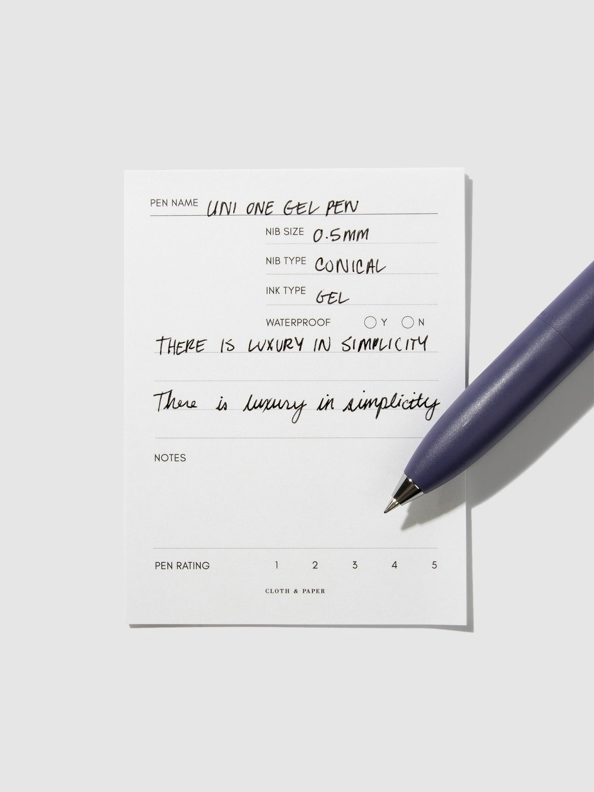 Uni-Ball One P pen resting on a pen test sheet. The sheet shows the pens specs. Color pictured is Grape.