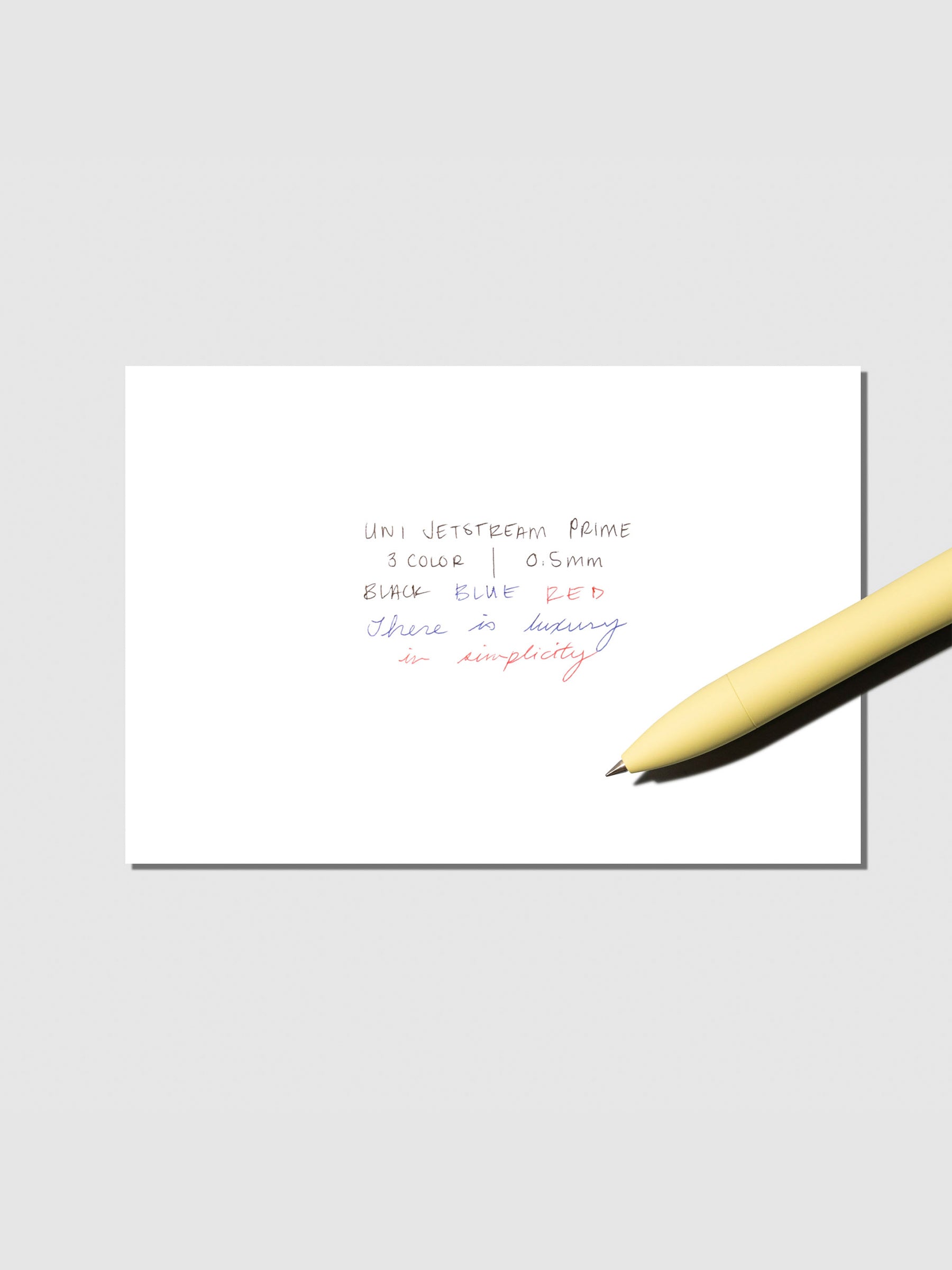 Writing sample with pen shown on a neutral background. Ink colors are black, red, and blue. Pen body color is Citron Yellow.