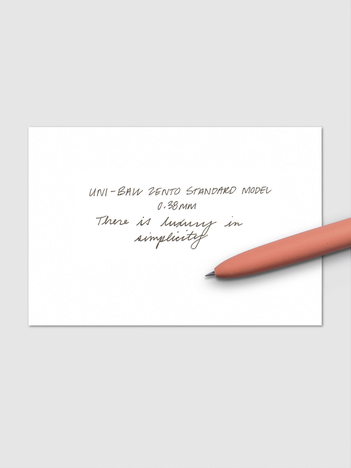 Handwritten sample using the Uni-ball Zento Standard Model Pen with black ink and a 0.38 mm nib. Shown with adobe pen resting across paper.