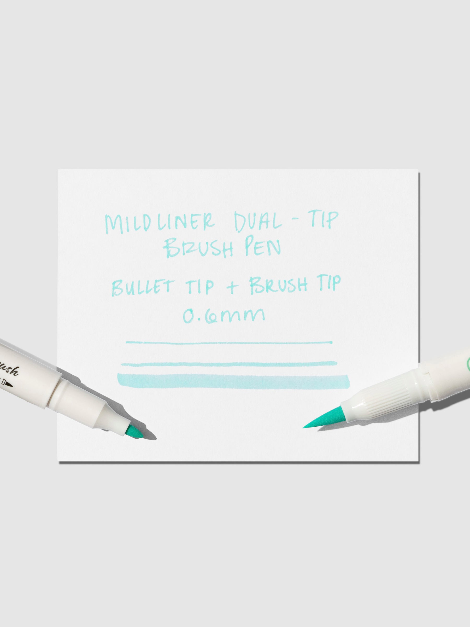 Brush pen tip resting on Blue Green pen test sheet displaying writing sample that details pen specs.