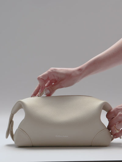 Woman using the Folded Form Pouch in the color Ristretto, an off-white, with planners and accessories